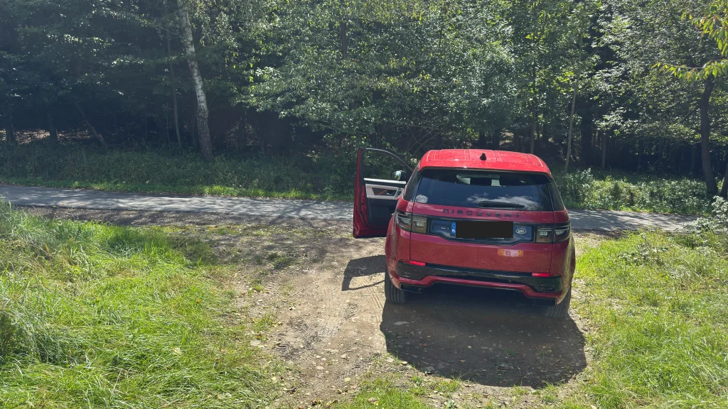 Samochód zaparkowany na utwardzonym wjeździe na teren, przy drodze gminnej.